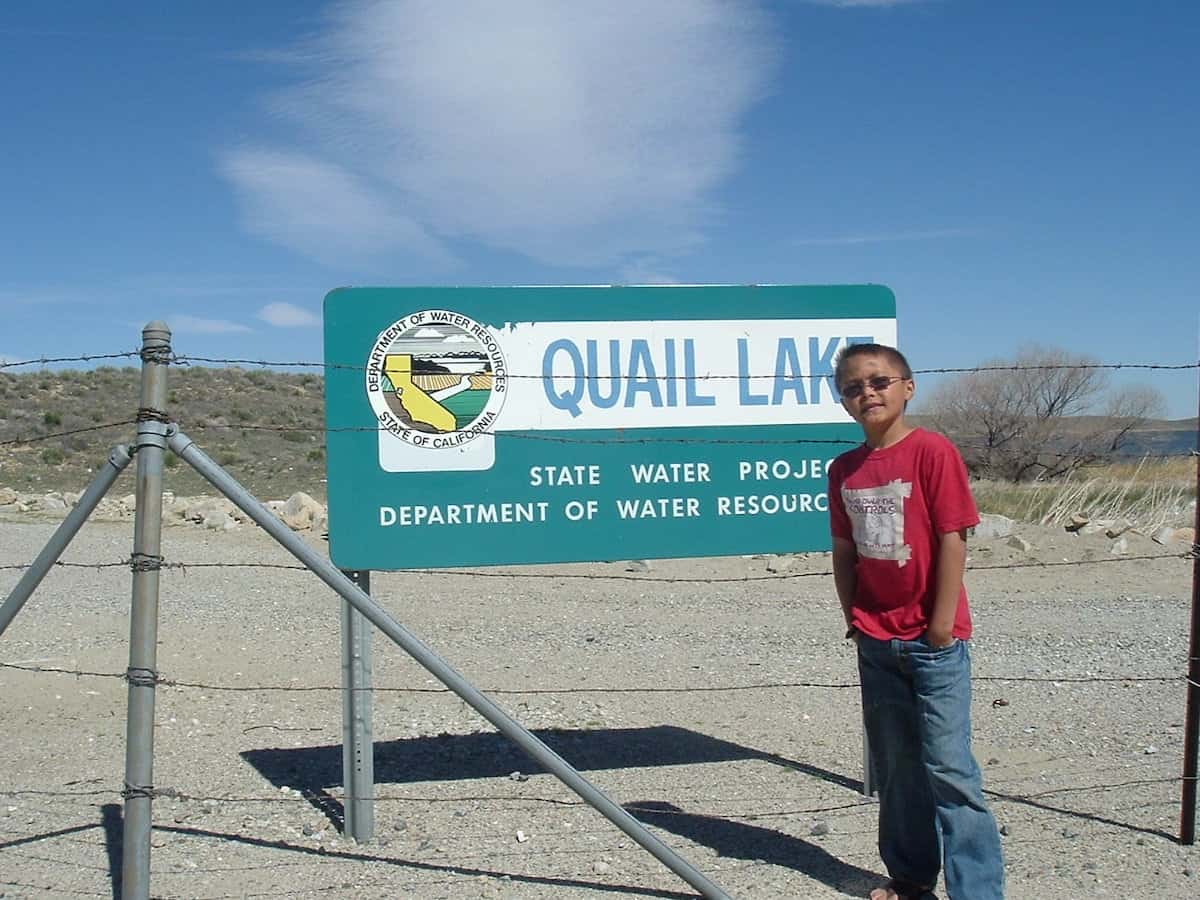 Boy stands near a sign at the entrance to Quail Lake, a fishing reservoir in Southern California.