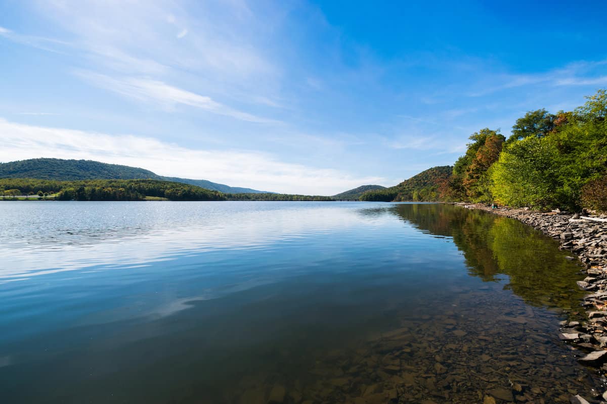 Blue water and sky frame the shoreline of trees and rocks along Raystown Lake in Pennsylvania.