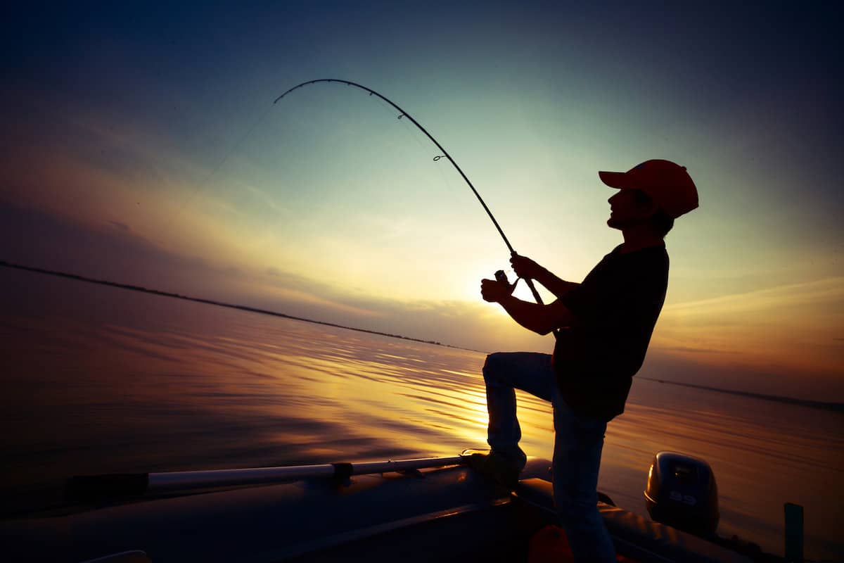 Silhouette of a boy or young man on a boat fighting a fish in the evening, the time when catfishing is best.