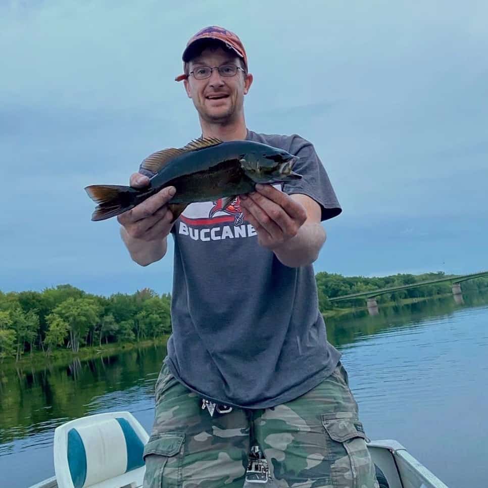 An angler holds a good sized smallmouth bass while standing in a boat on a Maine lake.