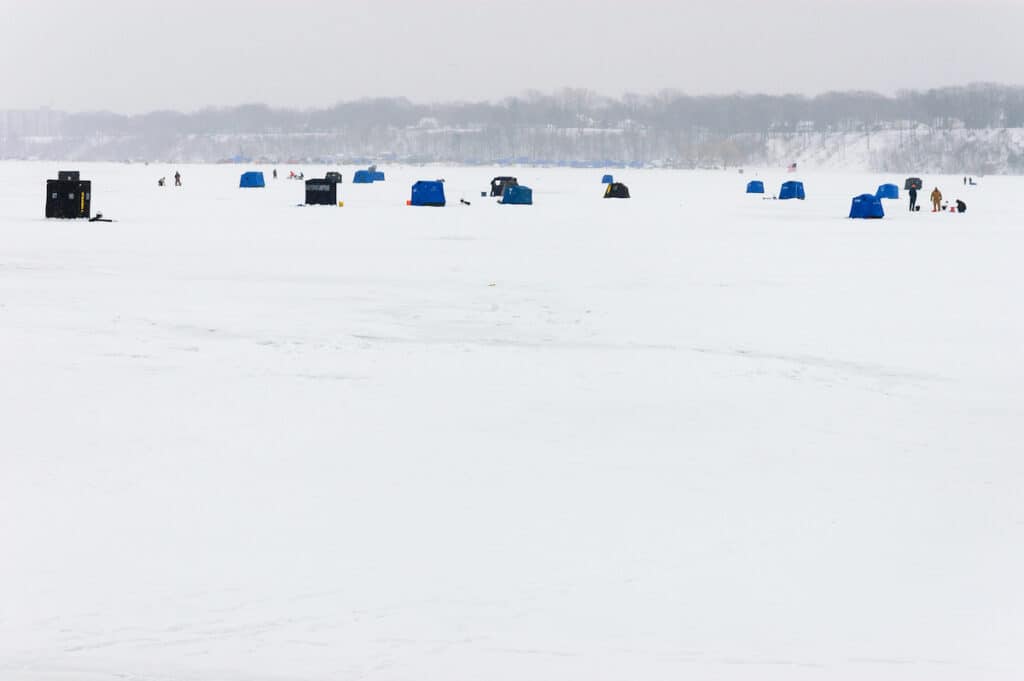 Ice fishing huts and individual people angling on the ice of Presque Isle Bay in winter.
