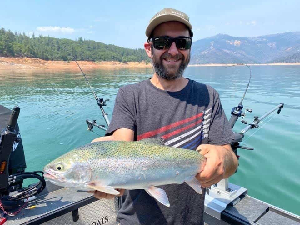 Angler holds a very large rainbow trout while bent rods in the back of the boat troll for more fish at Lake Shasta.