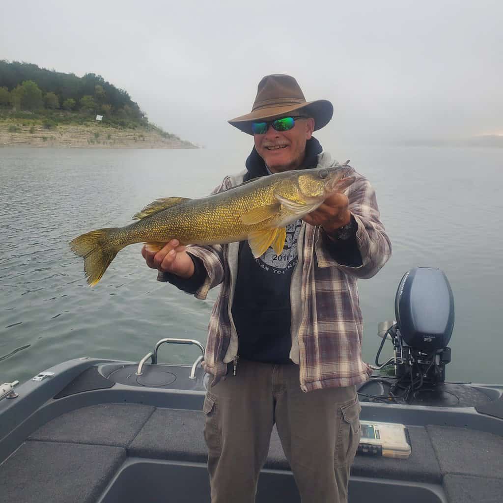 An angler wearing a hat holds up a nice walleye he caught fishing at Bull Shoals Lake on the border of Arkansas and Missouri.