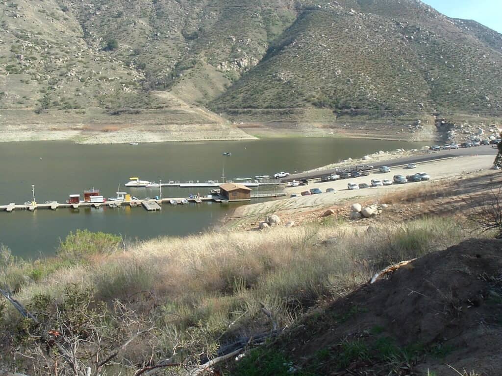 Distant view of boat docks and boat launch that anglers use to go fishing at El Capitan Reservoir, with dry hills of Southern California rising in the background.