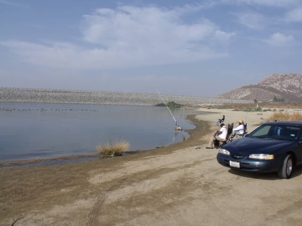 Anglers sitting in chairs next to a car while shore fishing for trout and other species at Lake Perris in Southern California.