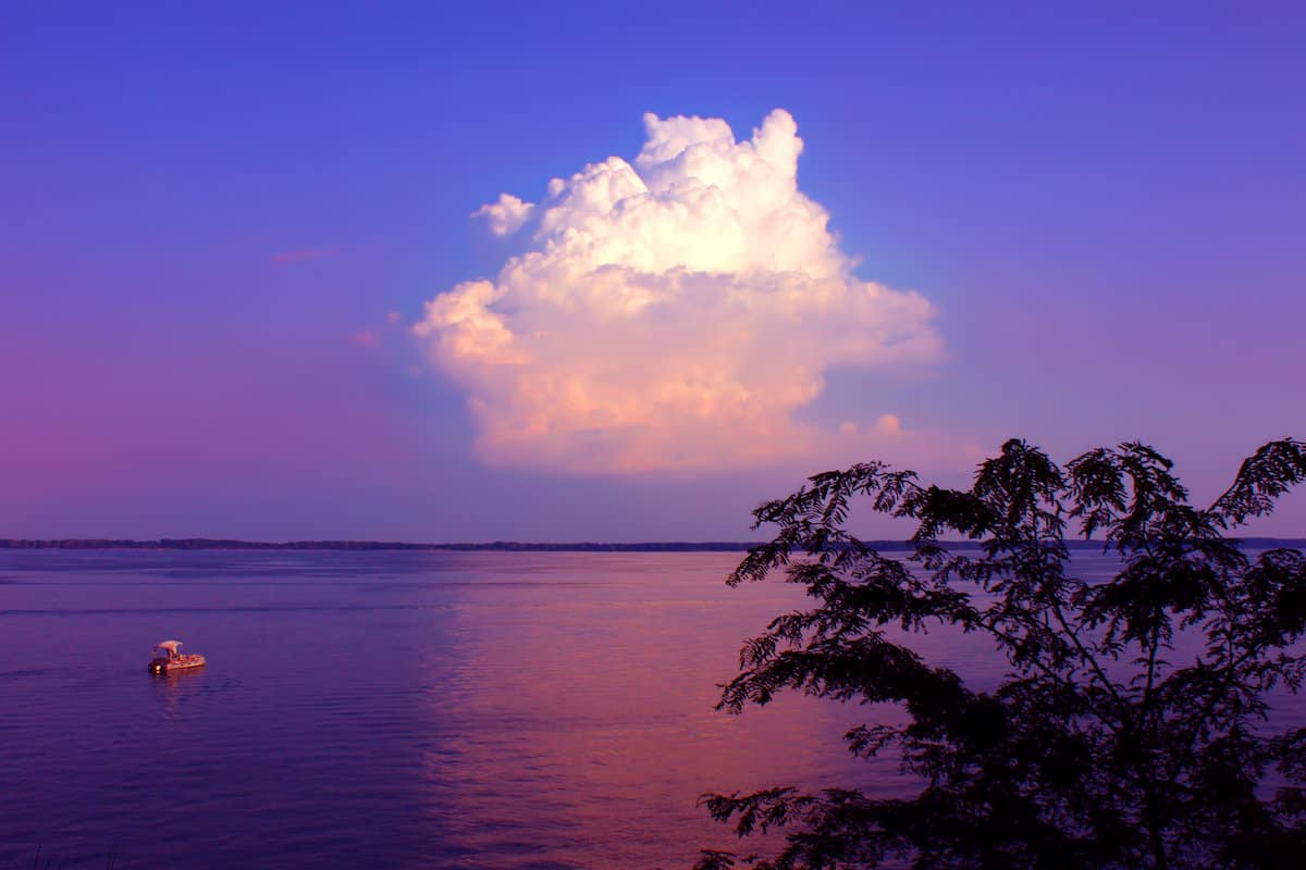 A fishing boat on the calm surface of Carlyle Lake with a white puffy cloud in a darkening blue sky.