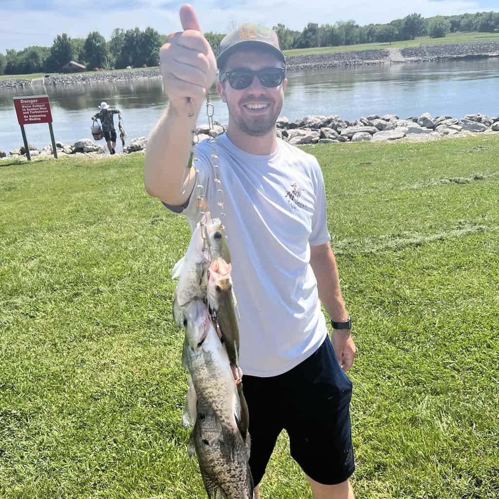 An angler gives the thumbs-up sign while holding up a stringer of crappie he caught fishing at Truman Lake in the background.