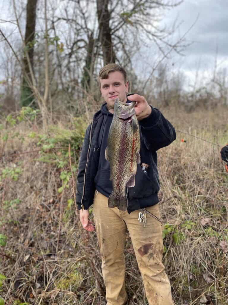 Standing man holds large hatchery rainbow trout caught in Cottage Grove Pond (Row River Nature Park).