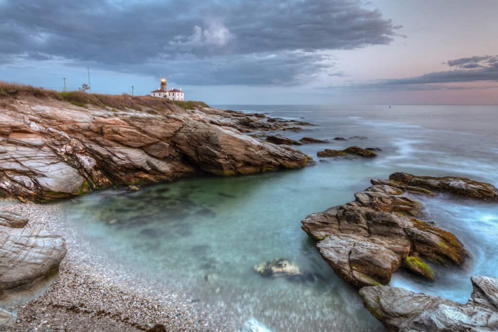 A long exposure photo of a rocky coastline at Beavertail Lighthouse at sunset near Jamestown in Rhode Island.
