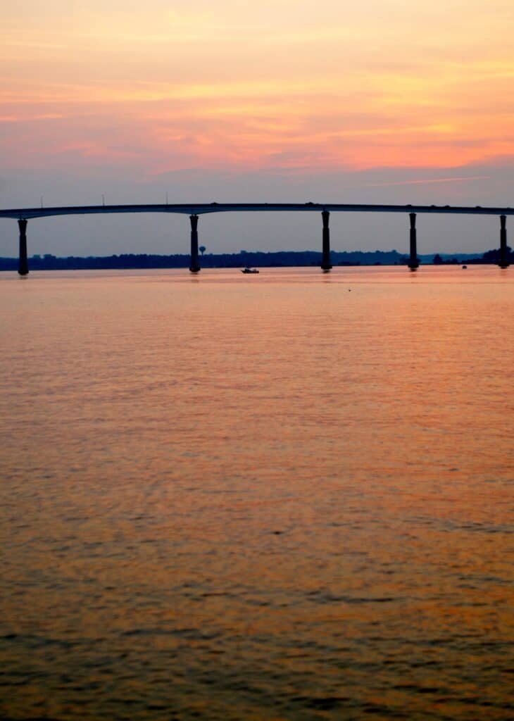 Orange sky reflecting on the Chesapeake Bay and Chesapeake Bay Bridge, with fishing boats beneath the bridge.