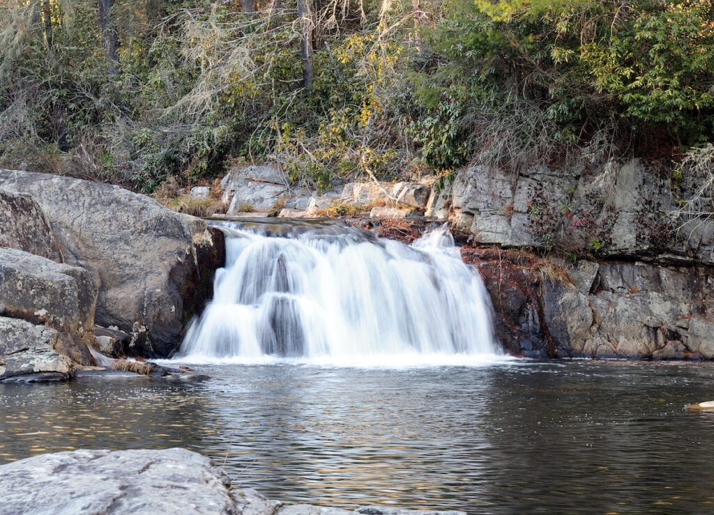 A low waterfall flows into a deep pool on the Linville River, making an excellent trout fishing spot.