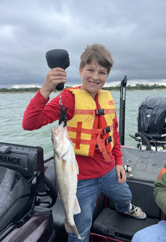 A smiling boy on a fishing boat holds up a large walleye he caught fishing at Canton Lake in Oklahoma.