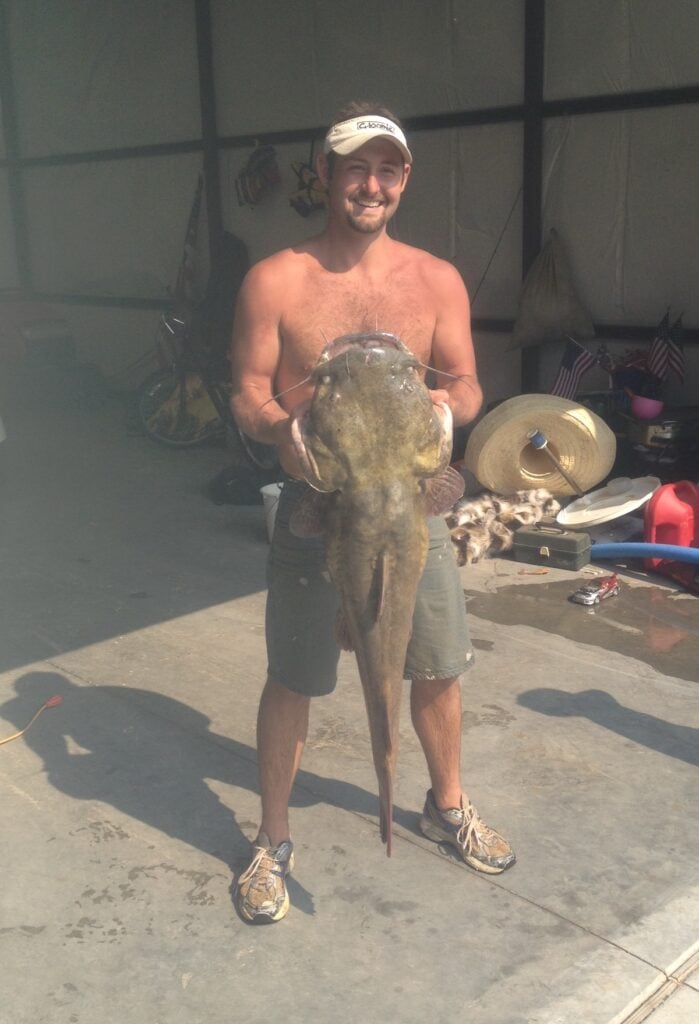 A shirtless angler holds up a massive flathead catfish he caught at Eufaula Lake in Oklahoma.