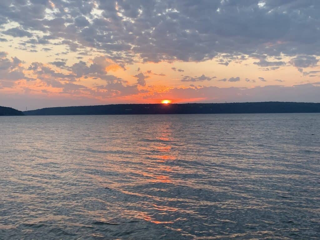 Bright orange sun rising over a distant hill with Eufaula Lake in the foreground.