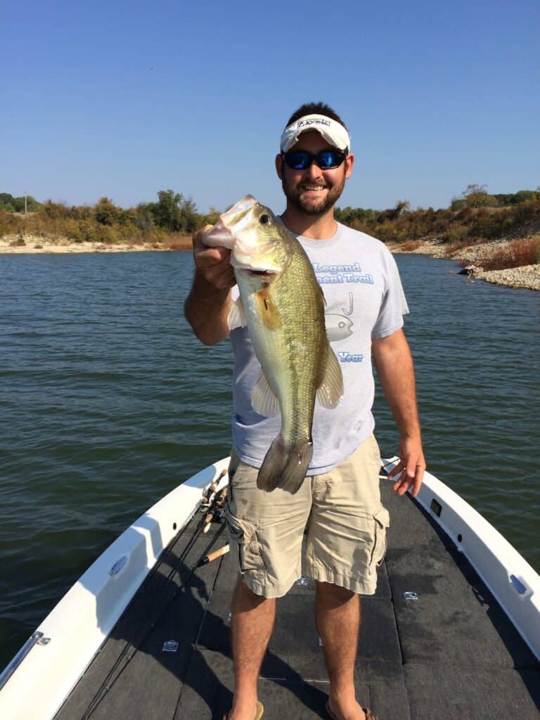 Smiling angler on a boat holding a trophy largemouth bass he caught fishing at Lake Texoma on the Texas and Oklahoma border.