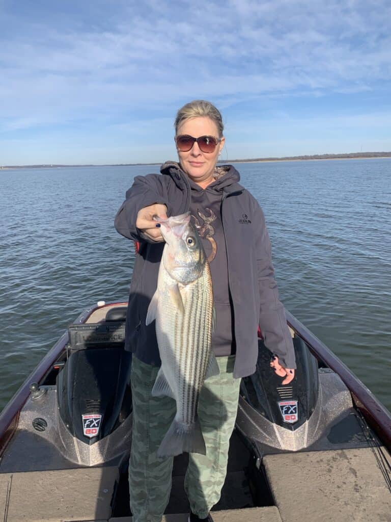 Woman in sunglasses holds a very large striped bass she caught while striper fishing on Lake Texoma.