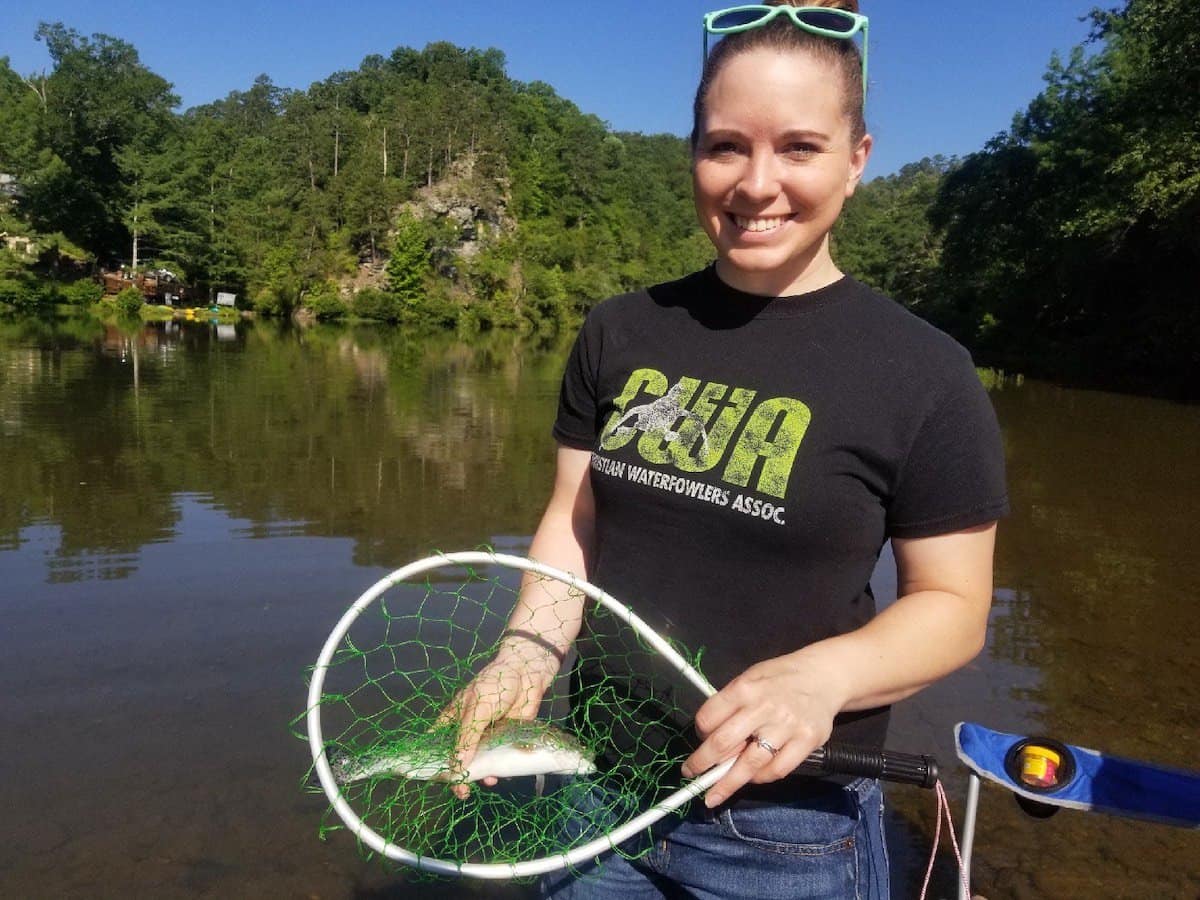 A female anglers holds a rainbow trout in a landing net she caught fishing at Lower Mountain Fork, which is in the background.
