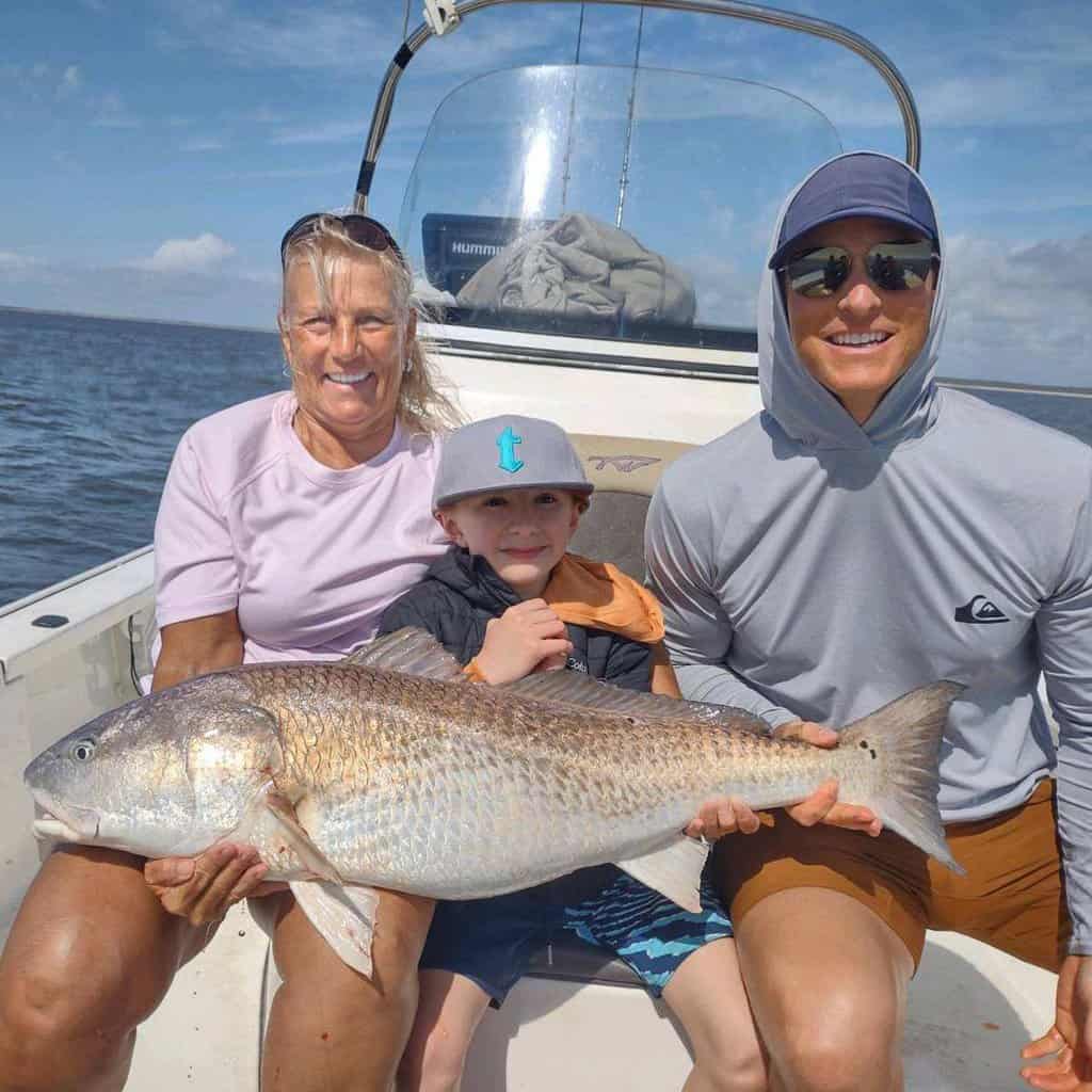A family of three holds a giant redfish on Captain Tommy Scarborough's boat in Georgetown, South Carolina.