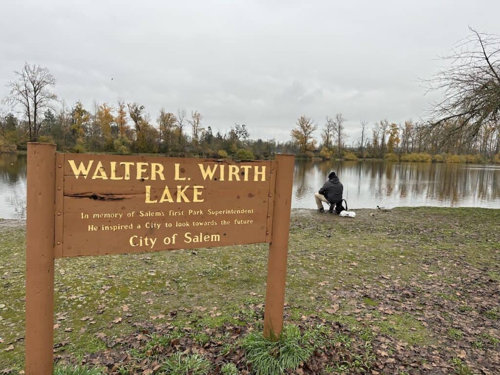 The sign at Walter L. Wirth Lake in Salem, Oregon, with a sitting angler on the shoreline in the background.