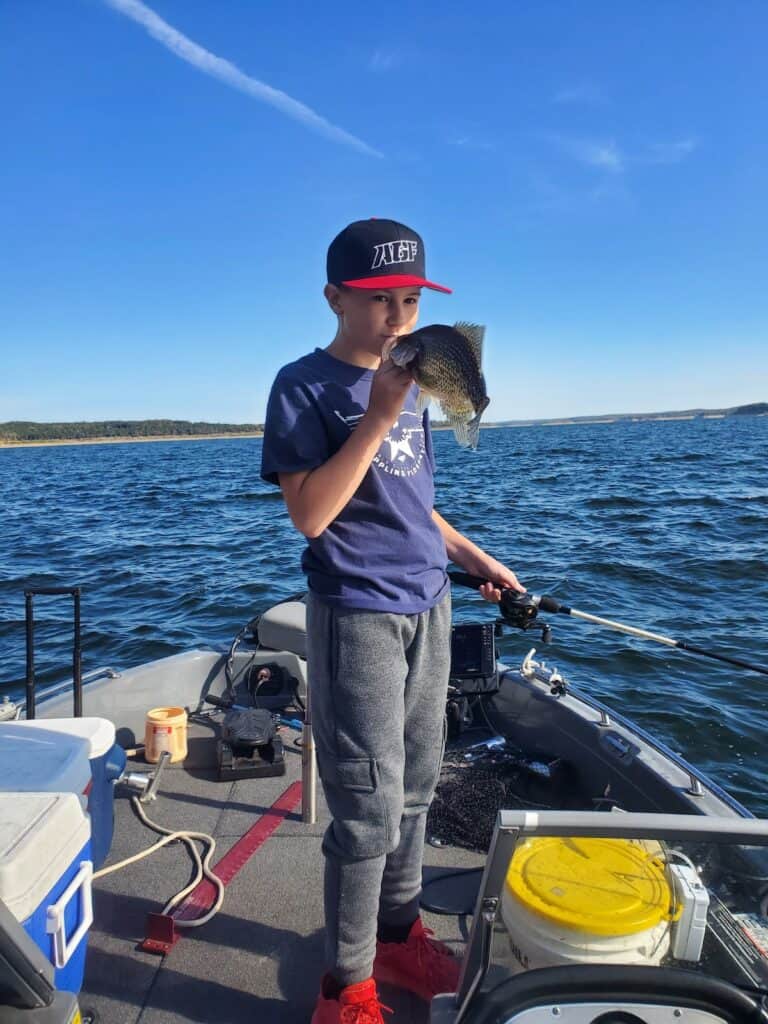 A boy holding a fishing rod kisses a crappie he just caught at Bull Shoals Lake in Arkansas.