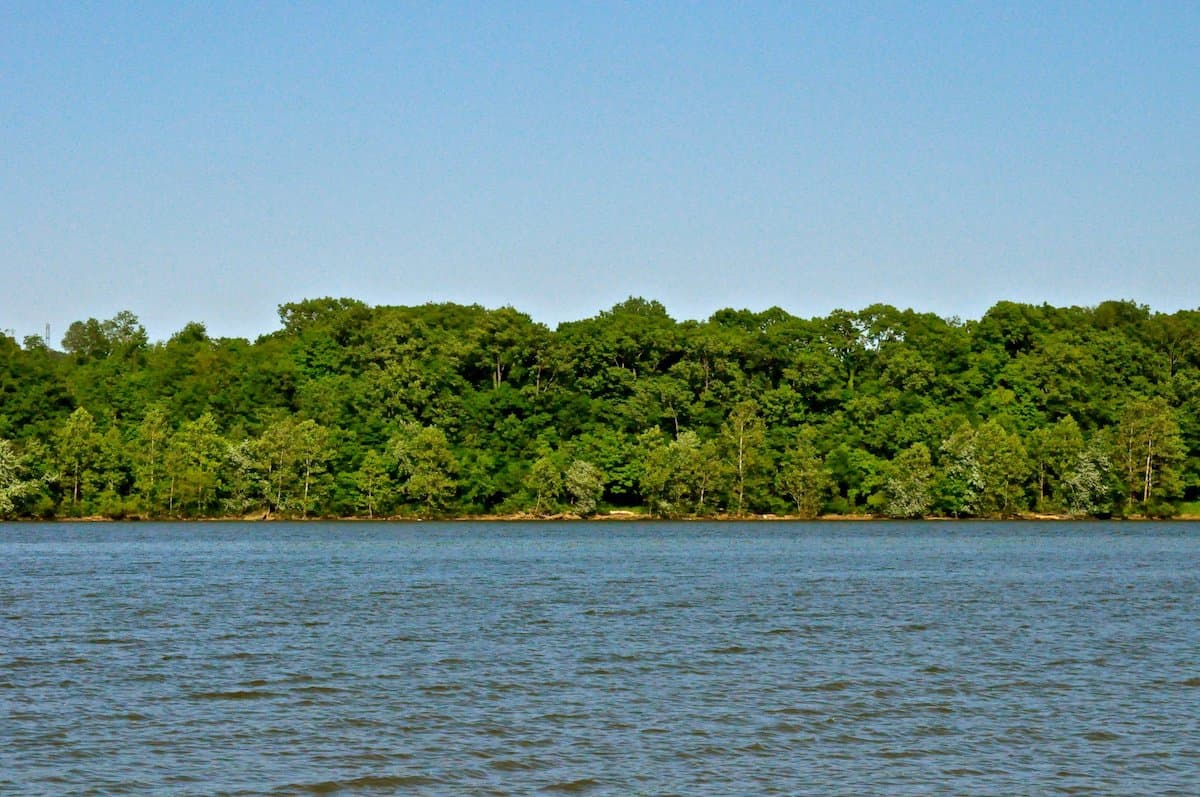 Blue water of the Ohio River under blue skies portends good catfish fishing, with trees in the distance.