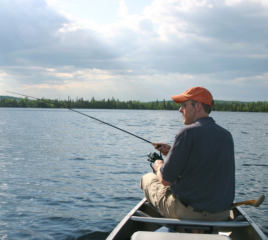 Man in red cap fishing in a canoe on a lake in Minnesota.