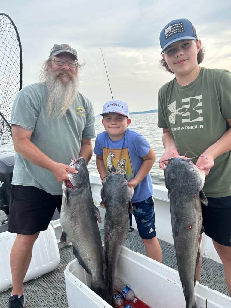 A bearded man and two boys on a boat each hold up big blue catfish they caught near the mouth of the Susquehanna River in Maryland.