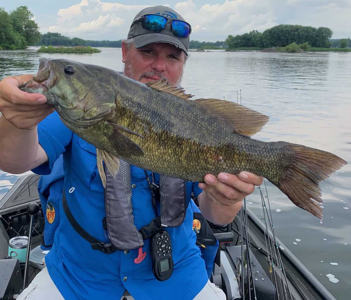 Man on a boat holds up a large smallmouth bass he caught fishing on the lower Susquehanna River.