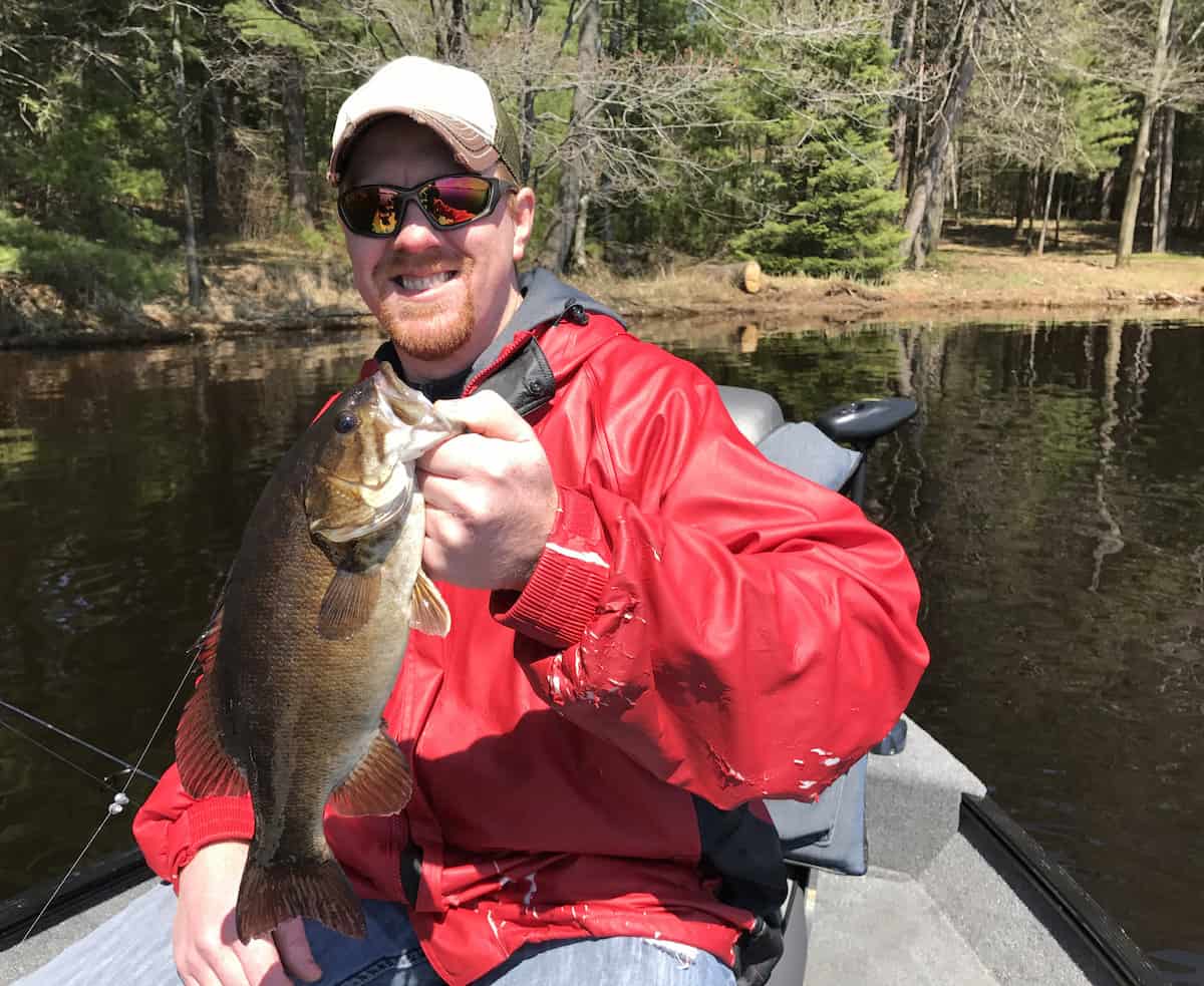 Fisherman sitting in a boat holds up a trophy Smallmouth Bass.